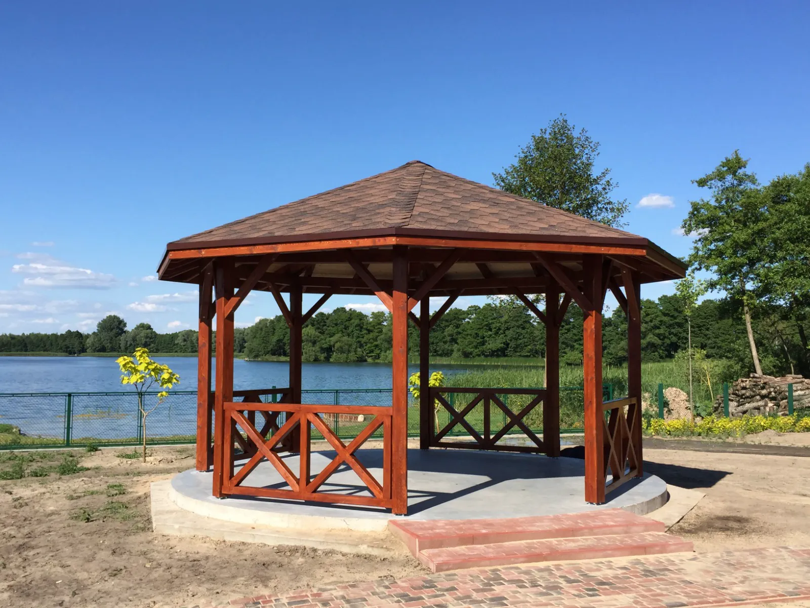Drewniana altana ogrodowa o ośmiokątnej konstrukcji z prefabrykowaną więźbą dachową nad jeziorem